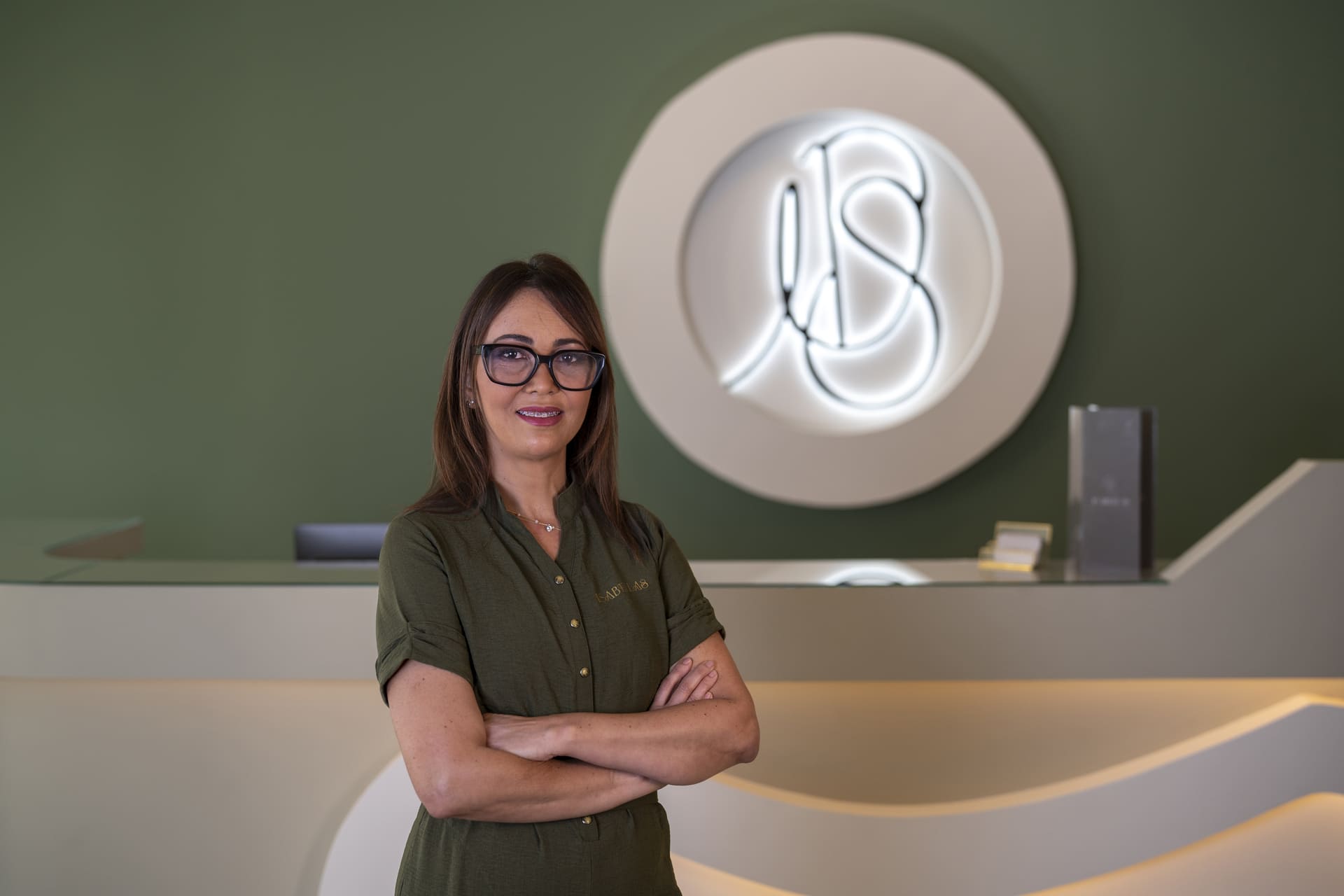 Mujer-brazos-cruzados-sonriendo-fondo-verde-logo-Isabellas-estética